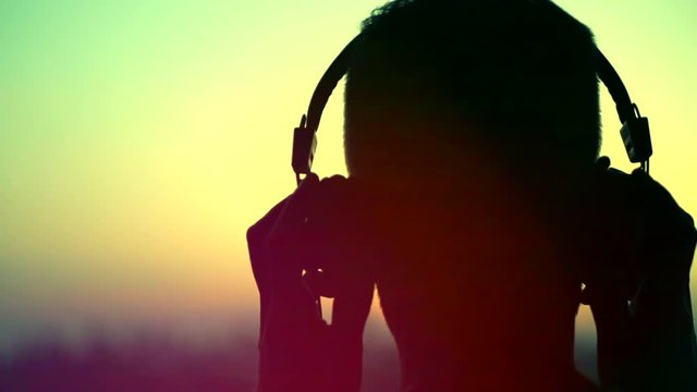 Young man wearing headphones, listening to music and looking on sunset city. Slow motion 240 fps. 4K UHD video 3840x2160