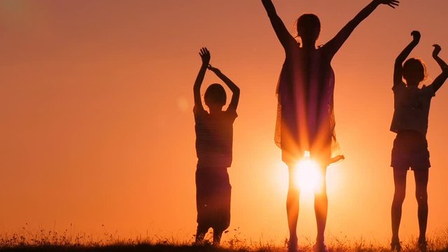 Mother and her children are jumping and waving their hands. The family is rejoicing and having fun at sunset.