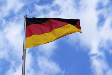 Flag of Germany with stripes in red, black and gold, national symbol or sign of the european country, fluttering in the wind against the blue sky with clouds on a sunny day