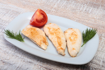 Slices of roasted chicken breast and tomato on white plate