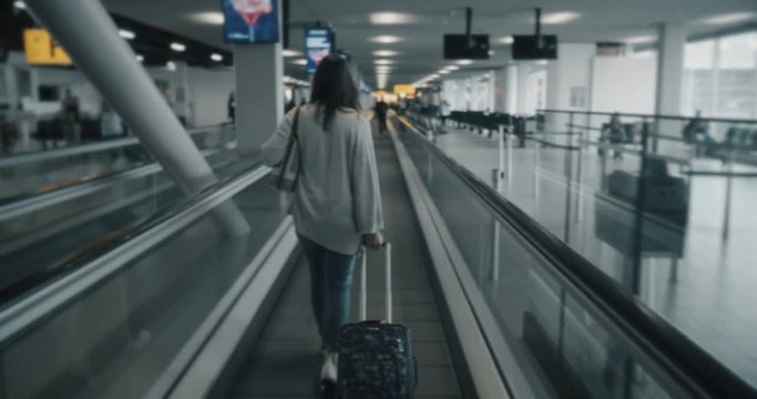 Woman using an airport walkway with suitcase in tow. (No discernible faces, all logos and trademark removed in post)