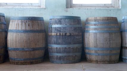 Fototapeta premium Old wood barrels lining a worn weathered wall in the basement of an old building. Used for food storage in early American history