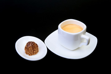 White cup of classic espresso coffee and pralines on black background.