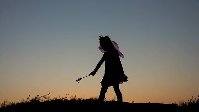 Silhouette of happy little girl dressed in a fairy costume with wings. The child presents himself as a sorceress, the concept of children's play and imagination.