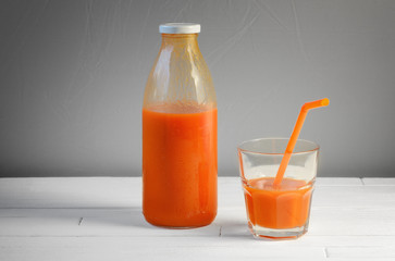 A bottle of carrot juice and a glass of carrot juice with a straw on white wood table. Still life of a healthy eating concept