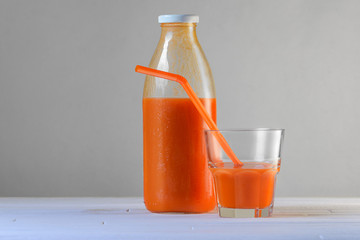 A bottle of carrot juice and a glass of carrot juice with a straw on white wood table. Still life of a healthy eating concept