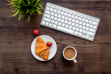 Dessert fo light lunch at workplace. Coffee, strawberry, croissant near keyboard on wooden background top view copyspace