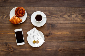 Pay bill at cafe by card. Bill and bank card near coffee and croissant on dark wooden table top view copyspace