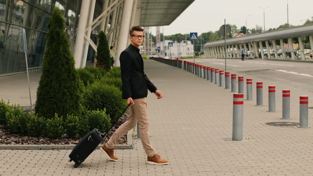 Stylish young business man with the baggage walking to the airport terminal to the lounge zone.