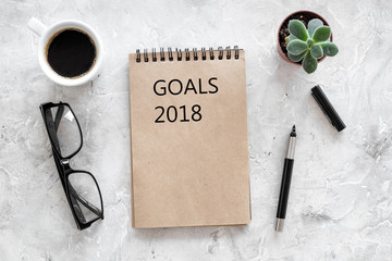 Words Goals for 2018 writting in notebook near glasses and cup of coffee on grey stone background top view mockup