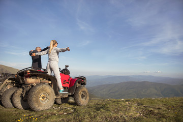 Beautiful couple is watching the sunset from the mountain sitting on quadbike