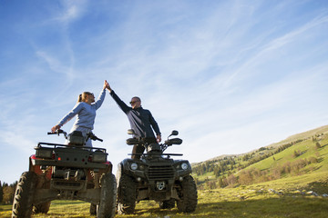 Obraz premium Beautiful couple is watching the sunset from the mountain sitting on quadbike