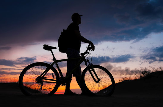 Silhouette of cyclist on the background of sunset. Biker with bicycle on the sand during sunrise