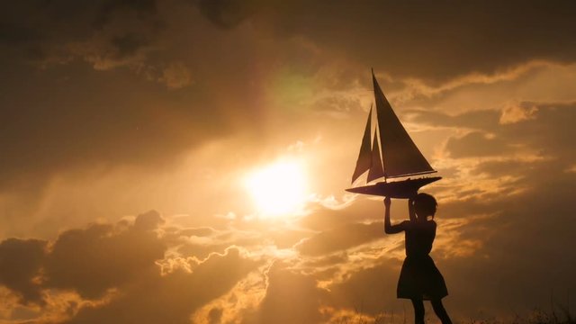 A child is holding a sailboat model against the sky. Beautiful sunset. Backlight.
