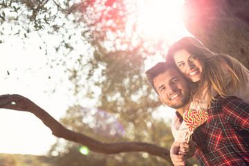 Portrait of smiling handsome man giving piggy back to his girlfriend in the nature