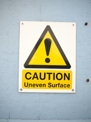 a close up caution uneven surface sign on blue wall seafront