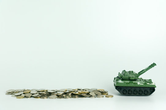 Green toy tank crossing over stack of coins isolated on white background, concept of expense and cost of war.
