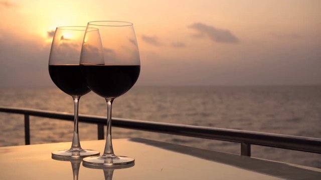 Romantic luxury evening on cruise yacht with winery setting. Glasses with red wine and tropical sunset with sea background, nobody