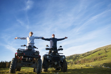 Obraz premium Beautiful couple is watching the sunset from the mountain sitting on quadbike