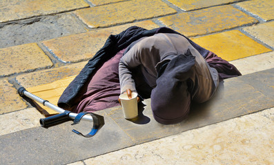 A woman in black clothes with a crutch begging for alms lying on the stairs