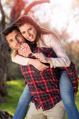 Portrait of smiling handsome man giving piggy back to his girlfriend in the nature
