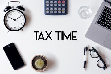 Tax Time words written on white table with clock, smartphone, calculator, pen, cactus, glass and laptop