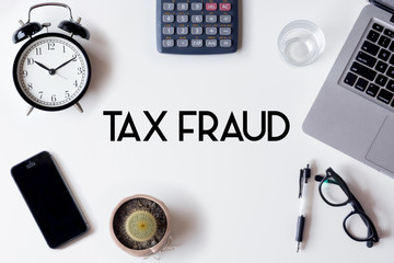 Tax Fraud words written on white table with clock, smartphone, calculator, pen, cactus, glass and laptop