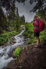 Obraz premium Hiking Colorado Girl Backpacker looks at cascading creek near lake Isabelle