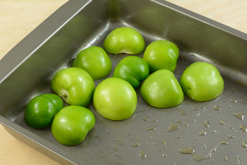 Raw tomatillo halves in baking pan with olive oil