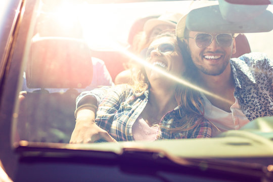 Group of happy young friends in cabriolet with raised hands driving on sunset