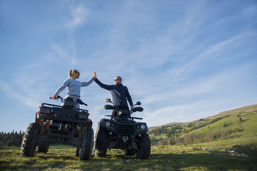 Obraz premium Beautiful couple is watching the sunset from the mountain sitting on quadbike