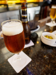 Close-up detail of an ale beer in a stemmed glass on a bar counter, with olives in ramekins as an appetizer. Vertical orientation. Valencia, Spain. Travel and drinks concept.
