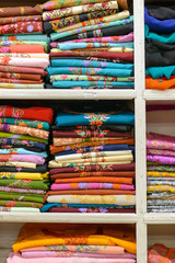 Close-up detail of wooden shelves stacked full of folded colorful Indian women's Pashmina designer clothing. Vertical orientation. Kashmir, India. Travel and fashion concept.