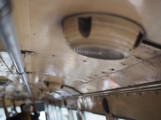 Side view dirty old round speaker on ceiling, with steel holding bar in Thai local public transport bus