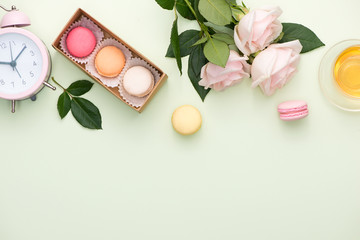 French macaroons. Many variegated sweet macarons in box with bouquet of pink roses on the table