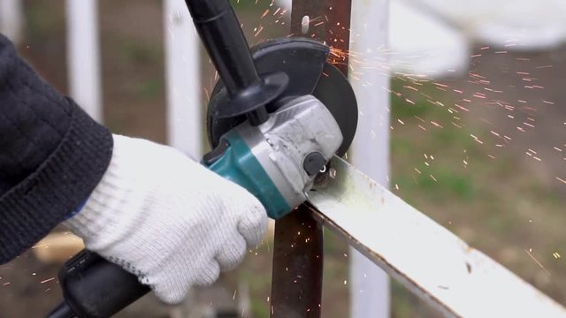 Worker in gloves cutting a steel rail with angle grinder