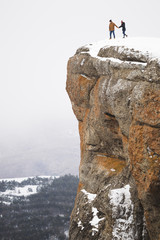 People standing on edge of mountain cliff, fog and snow around