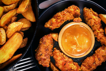 Chicken nuggets, fried potatoes and sauce on a black background. Top view