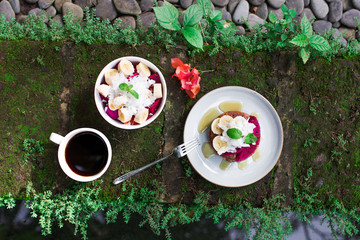 Tasty breakfast outside in garden. Fresh honey wholegrain pancakes with sliced dragon fruit, banana, coconut and mint. Cup of black Bali coffee