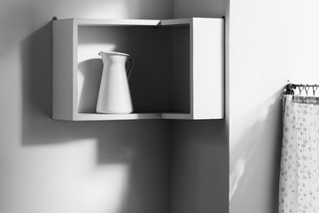 Minimalist interior of white modern kitchen. One isolated jug on shelf and light from window
