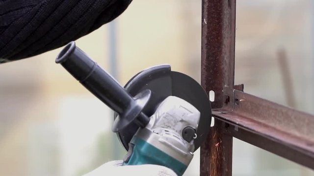 Worker in gloves cutting a steel rail with angle grinder