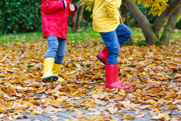 Closeup of kids legs in rubber boots dancing and walking through fall leaves