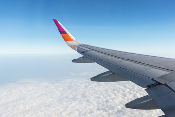 Fototapeta premium Wing of airplane flying above the clouds in the sky, looking through window