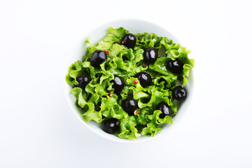 Green lettuce leafs with olive in bowl on white background
