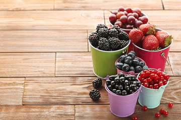 Ripe and sweet berries in buckets on wooden table