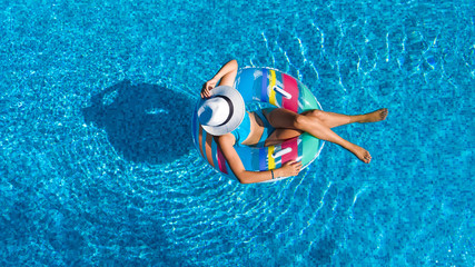 Aerial top view of beautiful girl in swimming pool from above, relax swim on inflatable ring donut and has fun in water on family vacation
