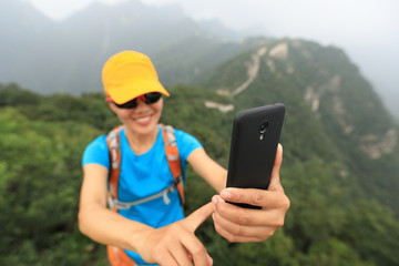 young woman hiker taking photo with smart phone on top of great wall