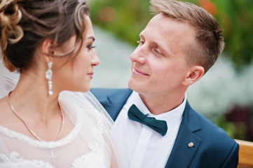 Elegant wedding couple sitting on a bench in the park and looking at each other's eyes.