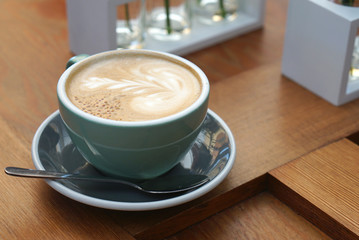 Hot cappuccino in green cup on timber table