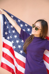 Fashion portrait of Hipster Asian woman wearing sunglasses and holding the American flag with smile.